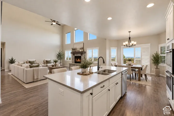 Virtually Staged: Open-concept living space featuring wood-finish flooring, a kitchen island with dual sinks, a stone fireplace, and vaulted ceilings