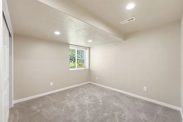 Recessed ceiling lighting, window with blinds, light gray wall paint, gray patterned carpet, and white trim molding