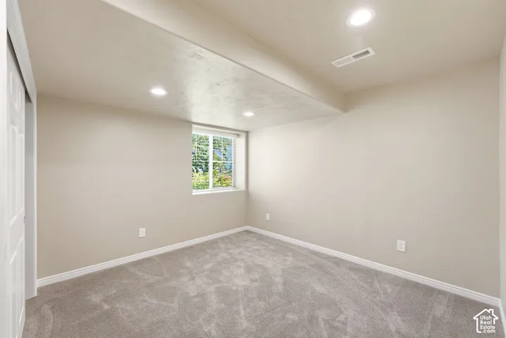 Recessed ceiling lighting, window with blinds, light gray wall paint, gray patterned carpet, and white trim molding
