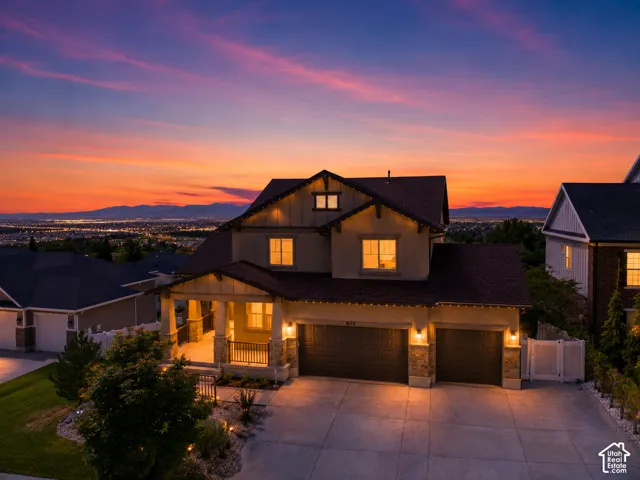 Stucco exterior with stone accents, covered front porch, attached double garage, paved driveway, and established landscaping