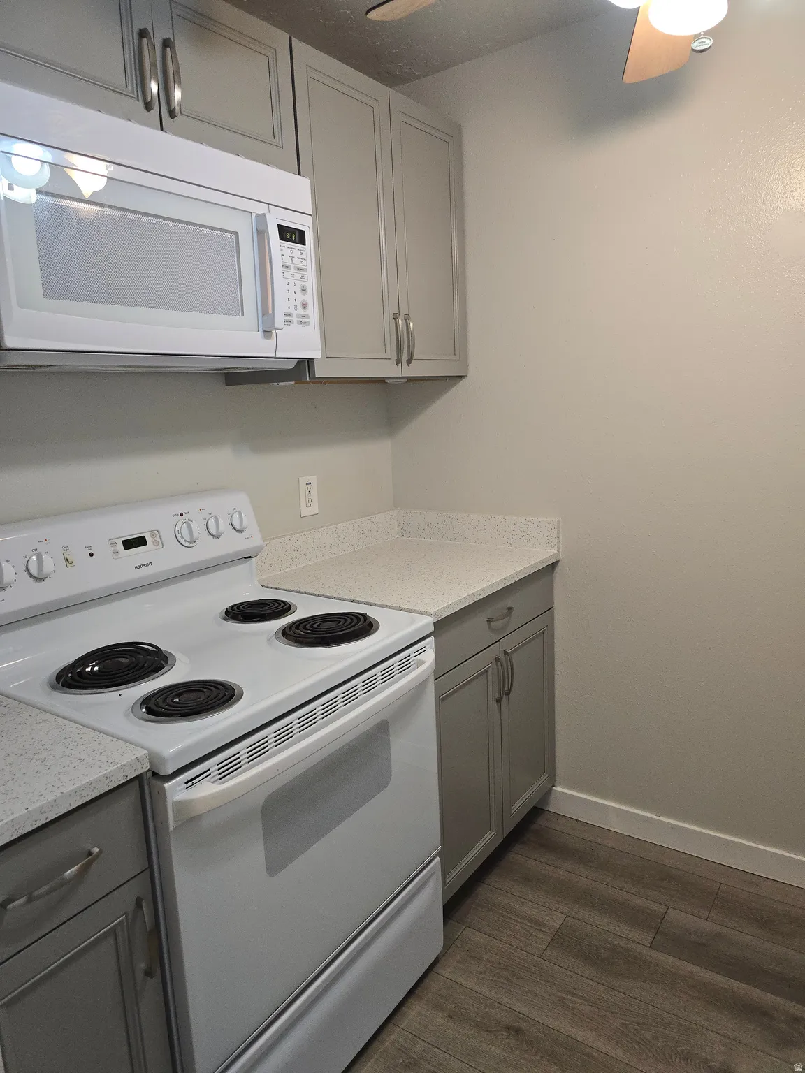 Light grey cabinetry, white countertops, built-in microwave, white electric range, and wood-finish flooring