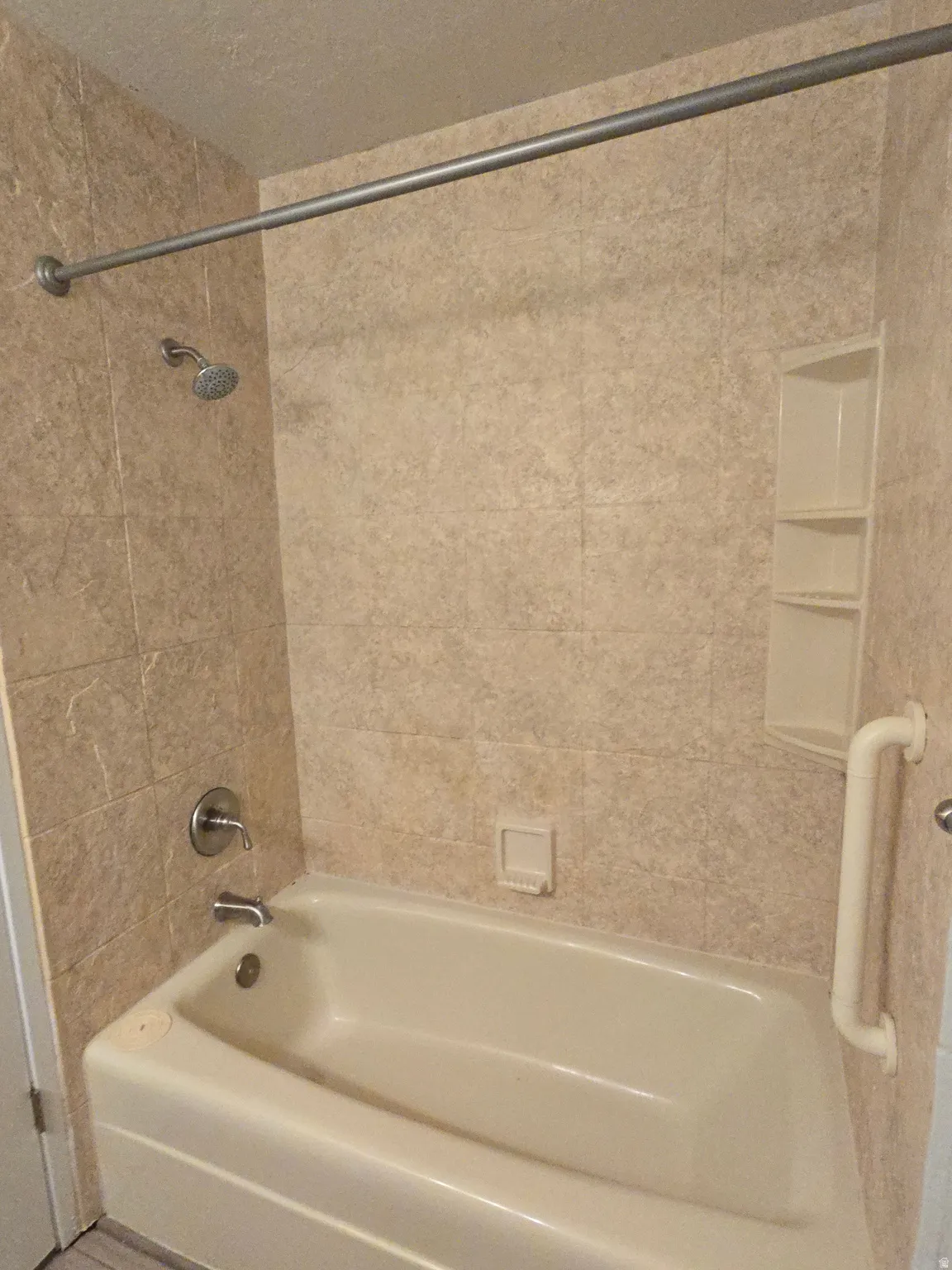 Bathtub with tile surround, built-in shelving, shower rod, and grab bar