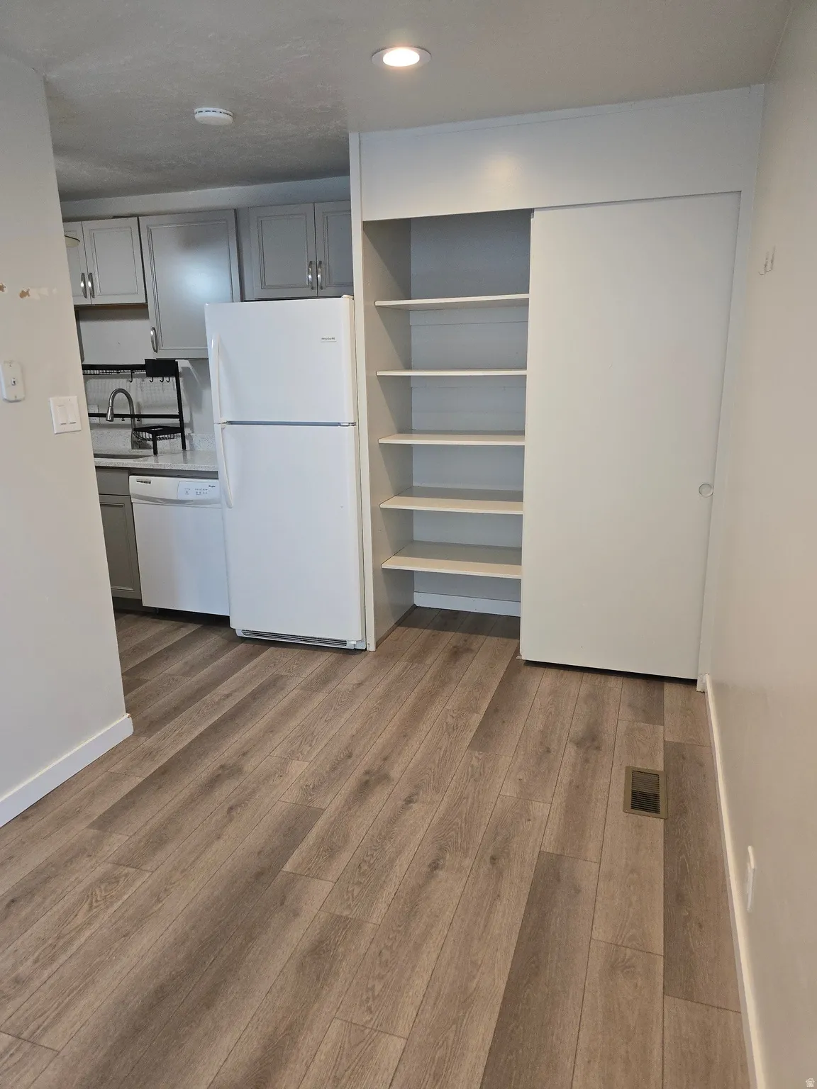 Wood-finish flooring throughout, recessed lighting, built-in shelving, and a full kitchen with white appliances and gray cabinetry