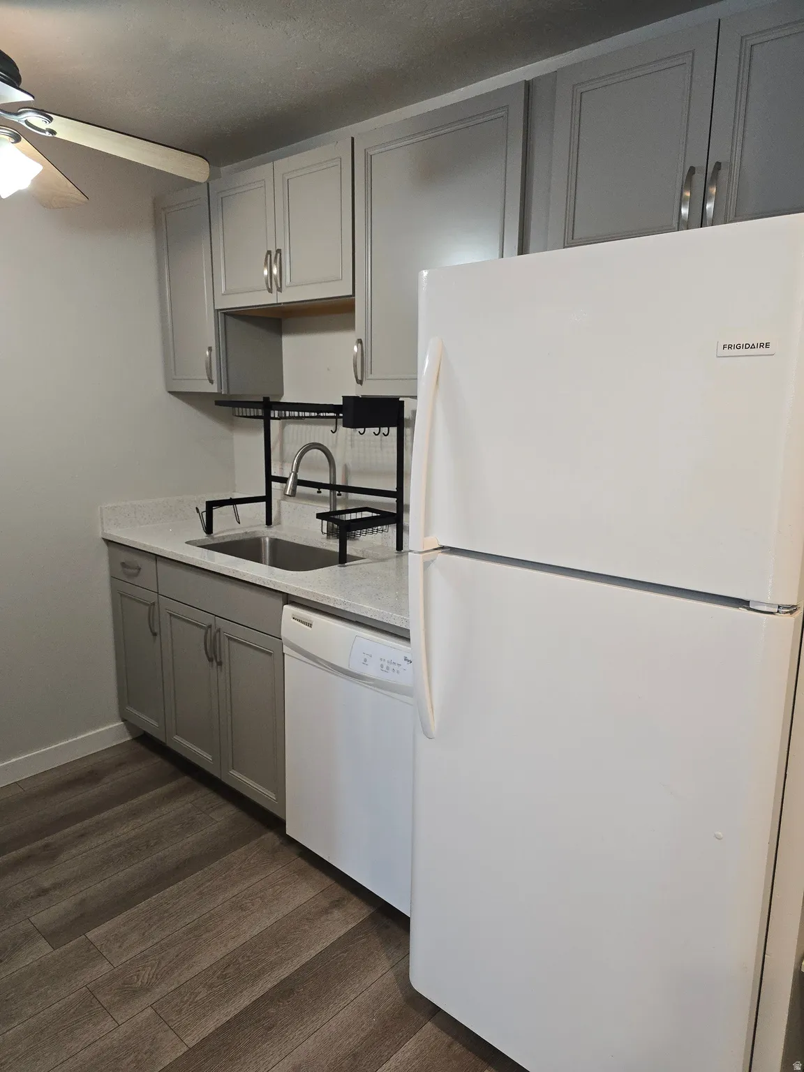 Kitchen featuring light gray cabinetry, white counter surfaces, stainless steel sink, white dishwasher, and wood-finish flooring