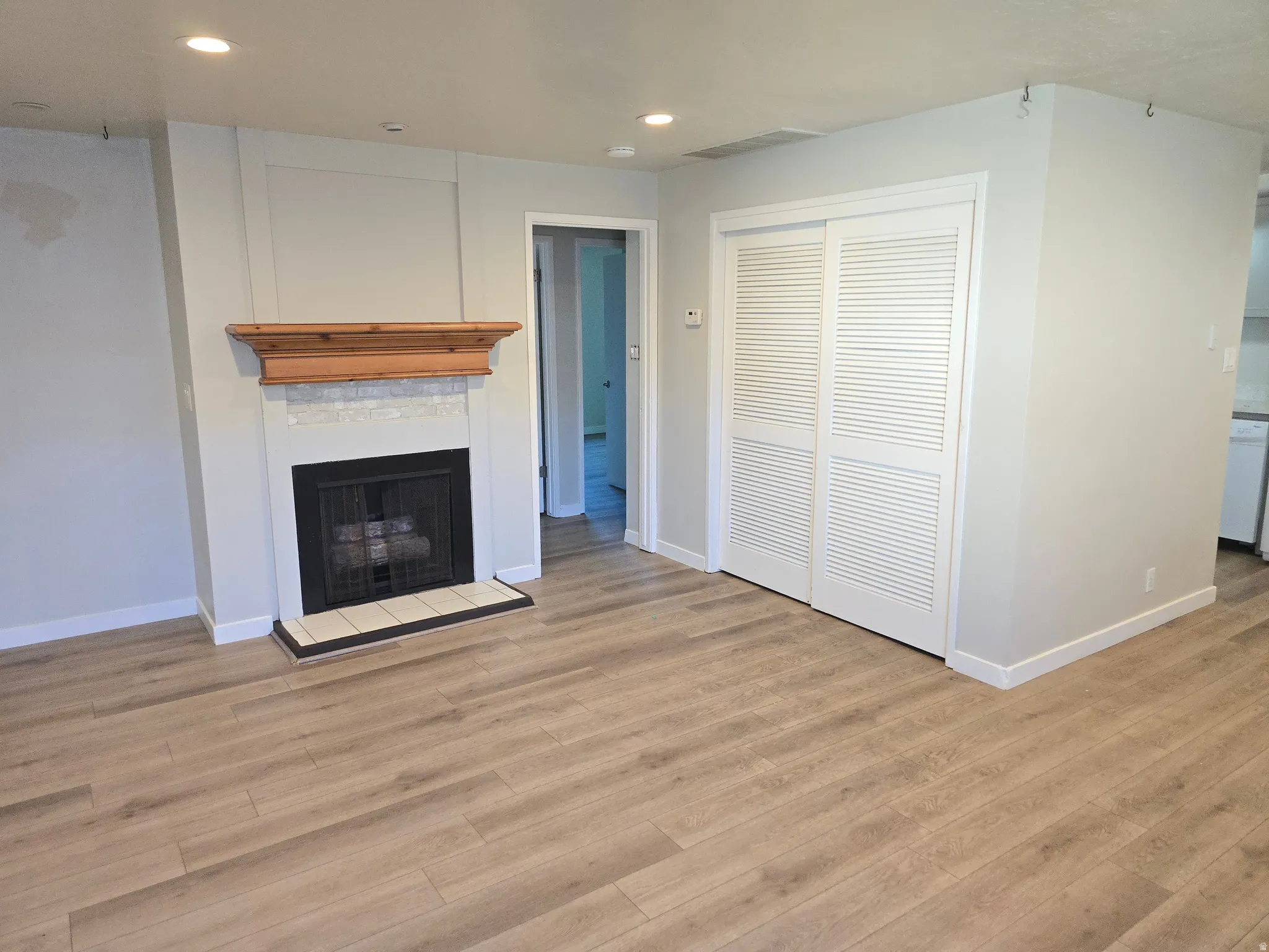 Wood-finish flooring, recessed lighting, and a fireplace with a wood mantle and tile surround
