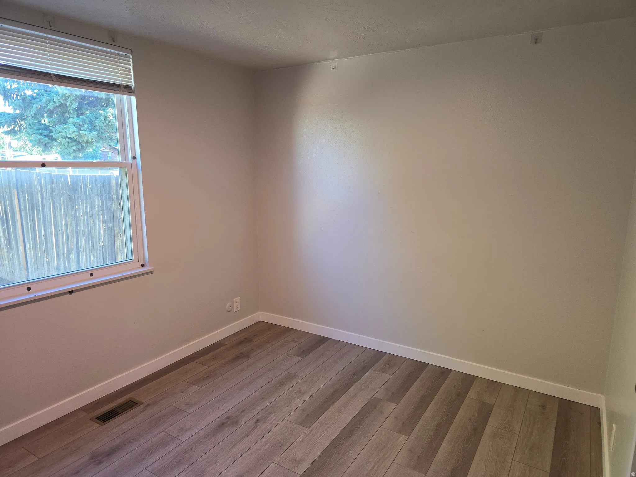 Window with blinds, wood-finish flooring, light neutral wall color, white trim