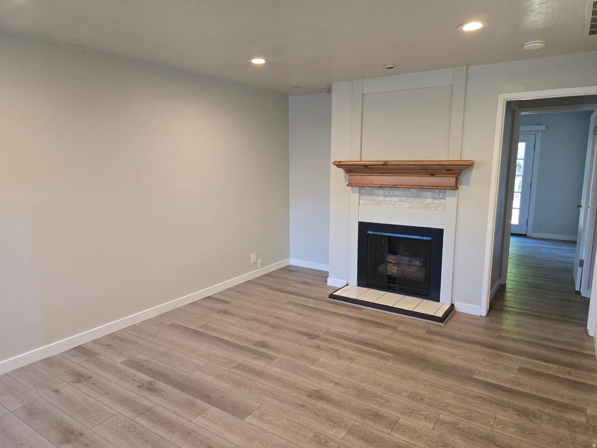 Neutral paint palette, wood-finish flooring, recessed lighting, fireplace with wood mantel, and tiled hearth