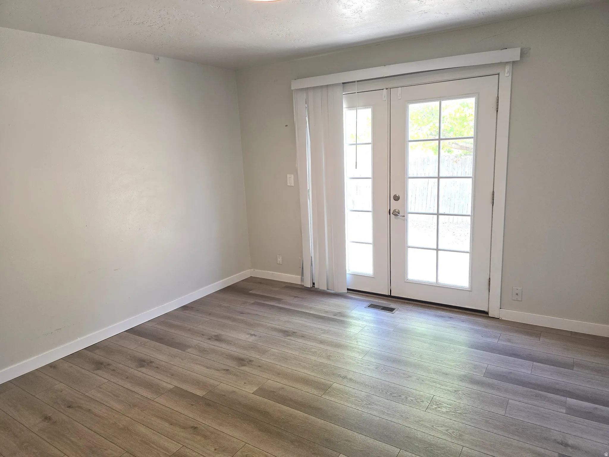 Wood-finish flooring, white walls, and white French doors with integrated window panes