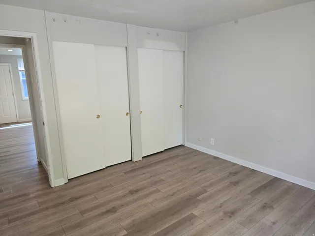 Wood-finish flooring, two sets of white sliding closet doors with brass-finish hardware, and light neutral wall paint