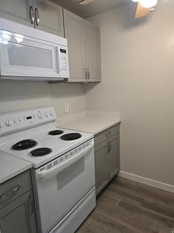 Light grey cabinetry, white countertops, built-in microwave, white electric range, and wood-finish flooring