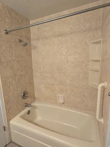 Bathtub with tile surround, built-in shelving, shower rod, and grab bar