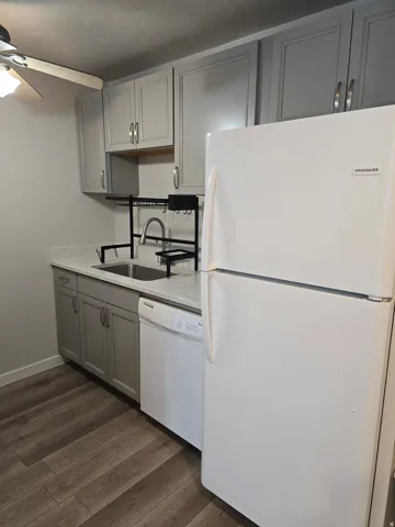 Kitchen featuring light gray cabinetry, white counter surfaces, stainless steel sink, white dishwasher, and wood-finish flooring