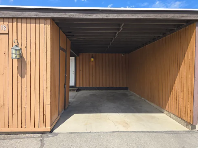 Carport entry with vertical wood paneling and concrete flooring, featuring an exterior wall sconce