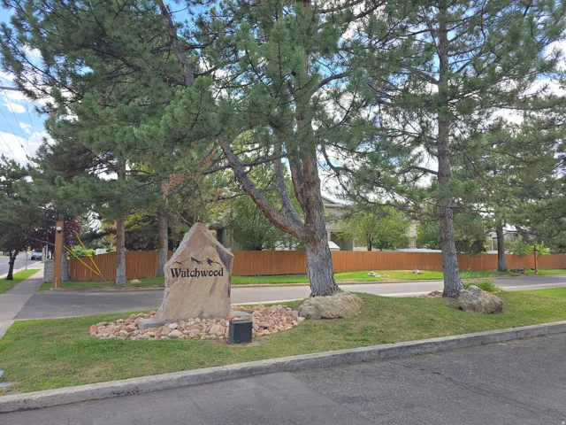 Stone community sign with decorative rock landscaping, mature trees, and a wooden perimeter fence