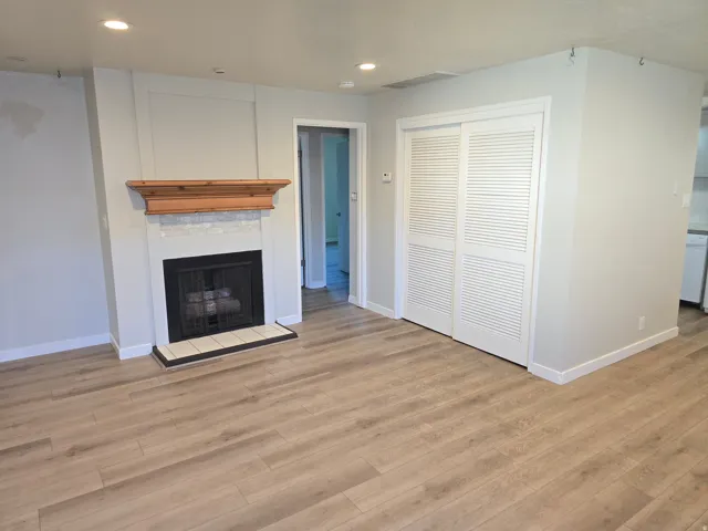 Wood-finish flooring, recessed lighting, and a fireplace with a wood mantle and tile surround