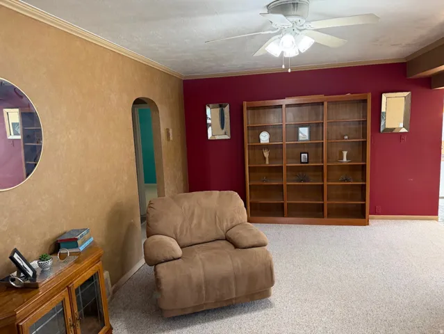 Archway entry, built-in shelving, ceiling fan light fixture, textured wall finish, and neutral carpet