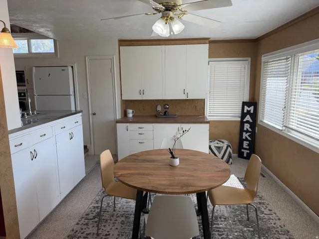 White cabinetry, built-in shelving, ceiling fan light fixture, two windows with blinds, and a built-in kitchen sink