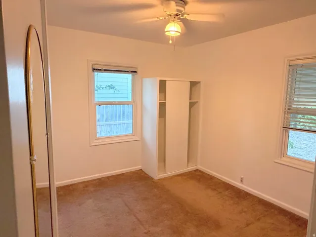 Carpeted room featuring a ceiling fan, two windows with blinds, and an integrated closet with sliding doors