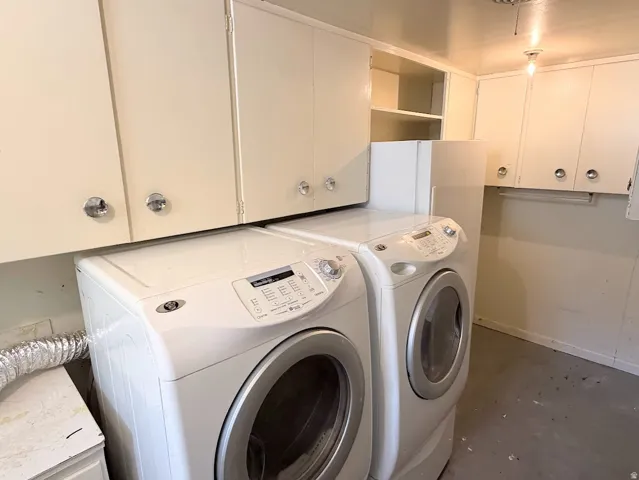 Laundry area with upper cabinetry featuring crystal-style knobs, shelving, and a concrete-finish floor