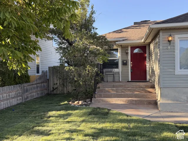 Red arched-panel front door, light gray siding, concrete steps, and a compact front lawn
