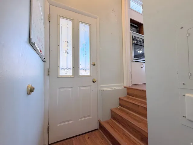 Entryway featuring a white door with decorative glass inserts, wood-finish stairs, and a built-in oven