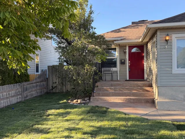 Red arched-panel front door, light gray siding, concrete steps, and a compact front lawn