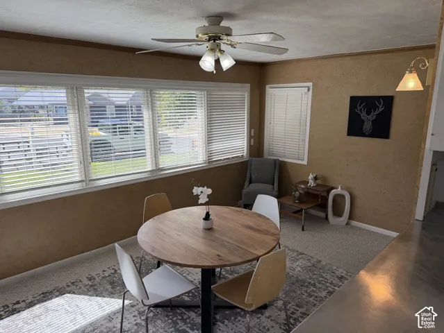 Dining area with multiple windows, textured wall finish, and a ceiling fan with integrated lighting