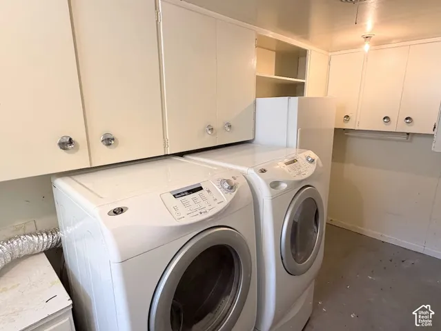 Laundry area with upper cabinetry featuring crystal-style knobs, shelving, and a concrete-finish floor