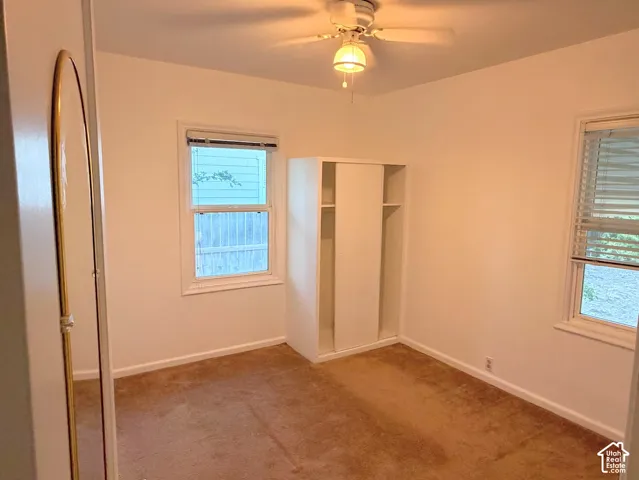 Carpeted room featuring a ceiling fan, two windows with blinds, and an integrated closet with sliding doors