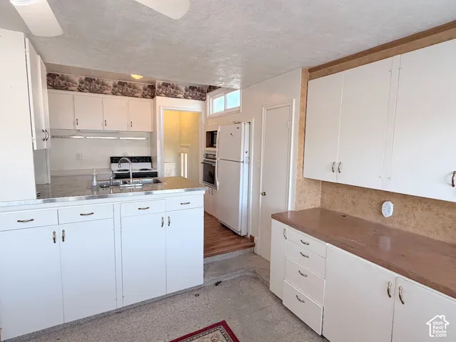 White cabinetry with chrome hardware, dual basin stainless steel sink, built-in wall oven, and wood-finish flooring