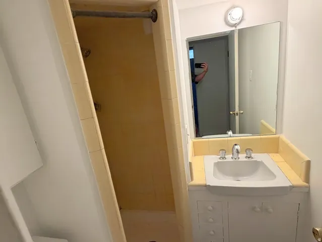 Integrated shower-tub combination, ceramic tile surround, vanity with storage, surface-mount mirror, and ceiling-mounted light fixture