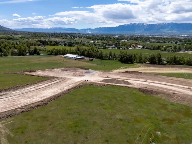 Expansive land parcel with visible excavation, surrounded by green fields and distant mountains