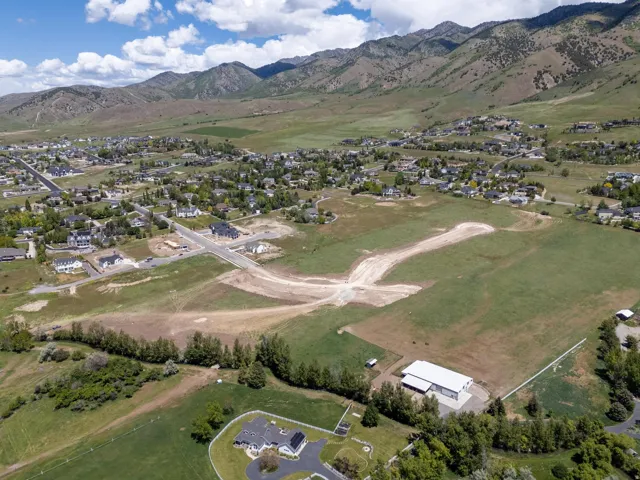 Expansive land parcel with graded roads, surrounding residential development, distant mountain backdrop, and existing structures