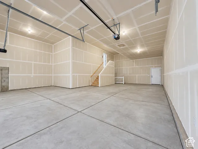 Expansive concrete flooring in a large unfinished garage space, featuring a staircase with wooden treads, a white paneled door, and exposed ceiling joists