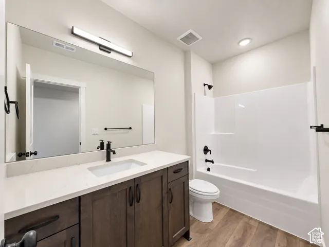 White quartz-finish countertop, wood-finish flooring, dark wood-finish vanity with storage, matte black fixtures, and a white integrated tub/shower unit
