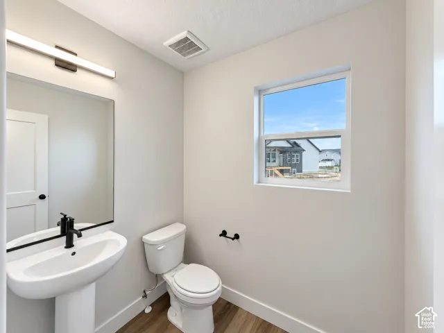 Pedestal sink with matte black faucet, rectangular mirror, modern linear vanity light, wood-finish flooring, and a single window