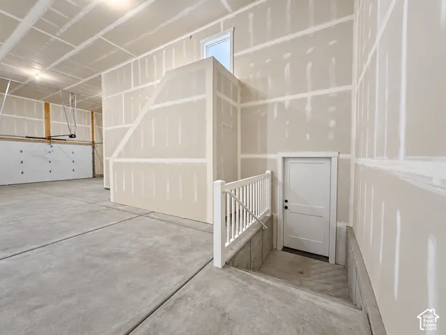 Concrete flooring with a white paneled door and matching white railing, featuring an overhead garage door
