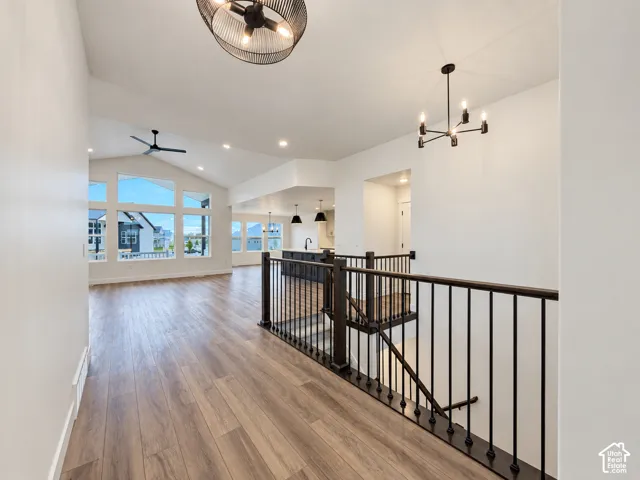 Vaulted ceiling with a ceiling fan, wood-finish flooring, black metal stair railing, and contemporary lighting fixtures
