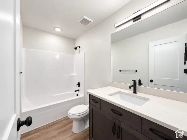 Bathroom featuring a dark wood-finish vanity with a light-colored countertop, an undermount sink with a matte black faucet, a white bathtub with a shower, and wood-finish flooring