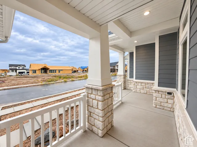 Covered front porch featuring white columns with stone bases, a concrete surface, white railing, and recessed lighting