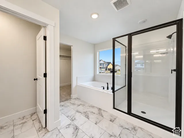 Spacious bath featuring large format tile flooring, a built-in tub with matte black fixtures, and a frameless glass shower enclosure with matte black accents