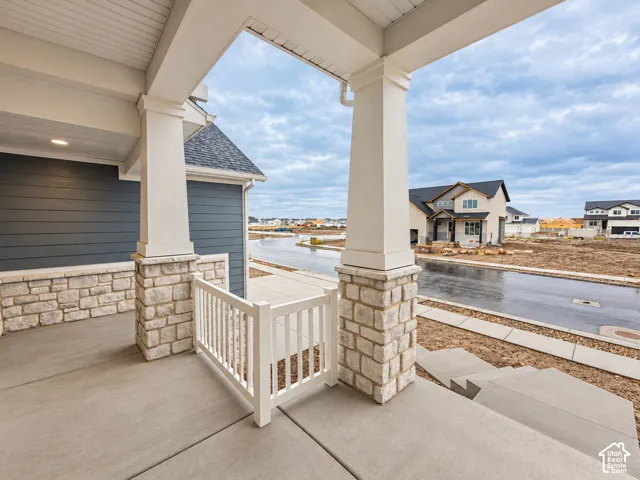 Covered front porch featuring stone-clad columns, a white railing, concrete steps, and a complementary siding facade