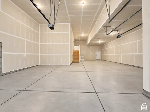 Spacious concrete flooring with integrated expansion joints, unfinished walls, ceiling-mounted lighting, and an exposed overhead garage door mechanism