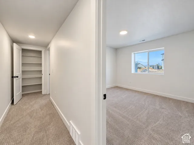 White walls, light-colored carpeting, a built-in shelving unit, and recessed lighting