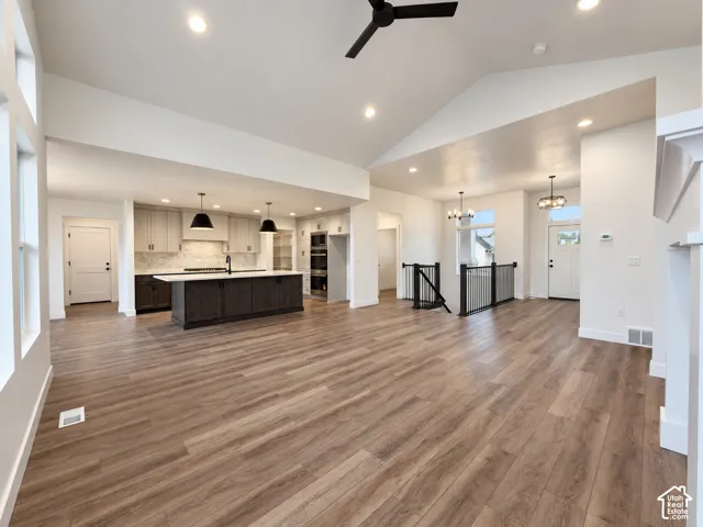 Spacious open-concept layout with vaulted ceilings, wood-finish flooring, and a modern kitchen featuring a dark island and light-toned cabinetry