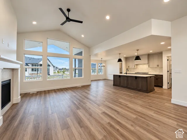 Vaulted ceilings with a ceiling fan, a fireplace with a tile surround, wood-finish flooring, and a kitchen island with pendant lighting