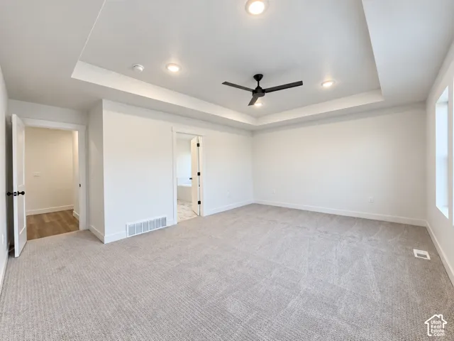 Tray ceiling with recessed lighting and a ceiling fan, light-toned carpeting, and a white interior door with dark hardware