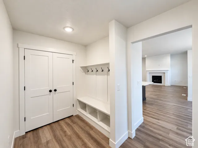 Recessed lighting, wood-finish flooring, built-in mudroom bench with storage, coat hooks, and a gas fireplace with a mantel