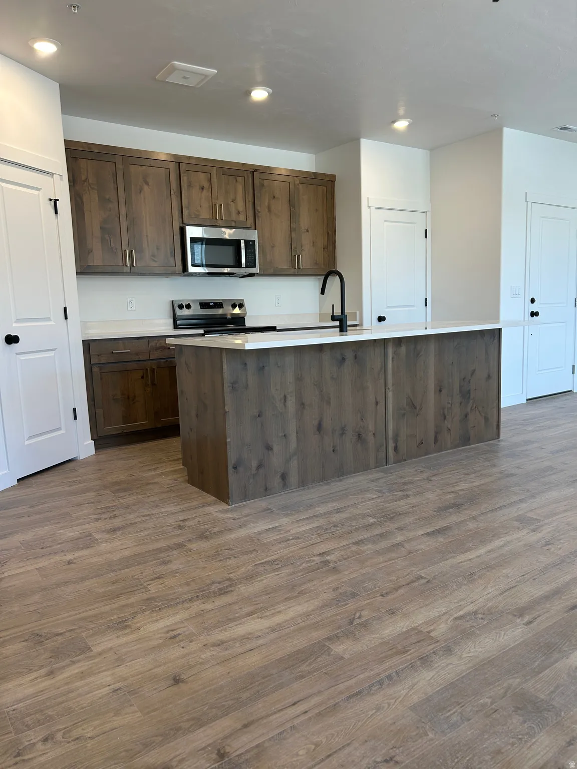 Kitchen featuring wood-finish cabinetry, stainless steel appliances, a center island with a white countertop, a matte black faucet, and wood-finish flooring