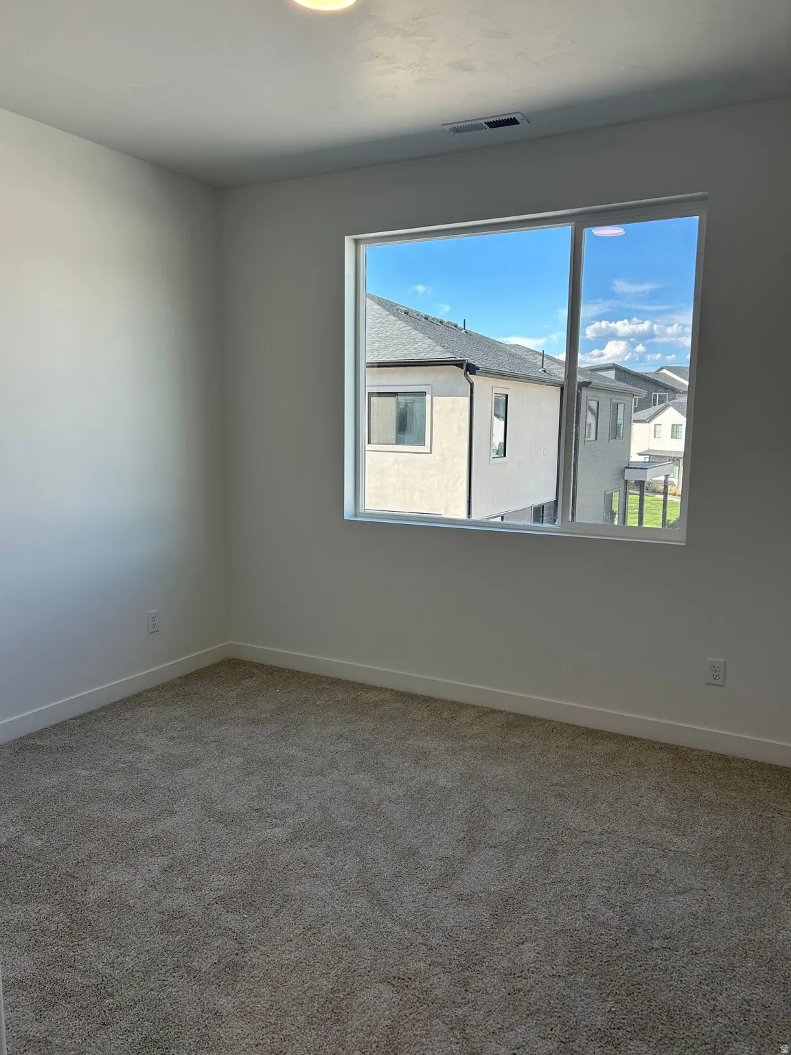 Neutral wall color, carpeted flooring, large window with white trim, recessed ceiling light